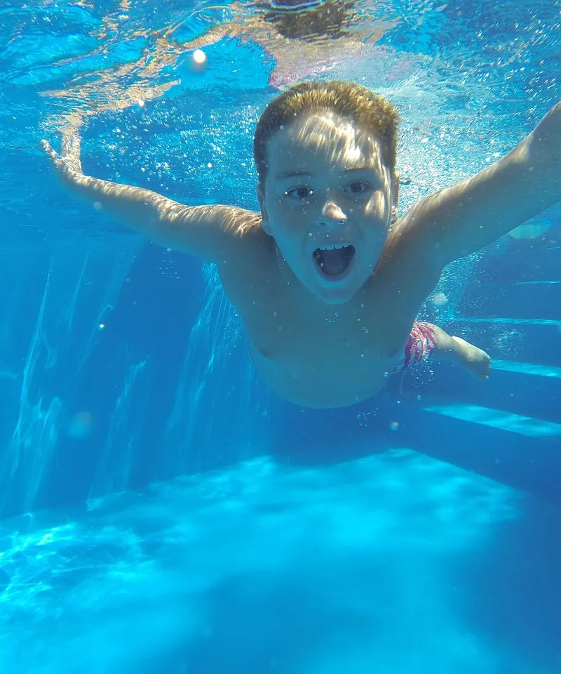 Kind taucht lachend mit ausgebreiteten Armen durch ein Schwimmbecken