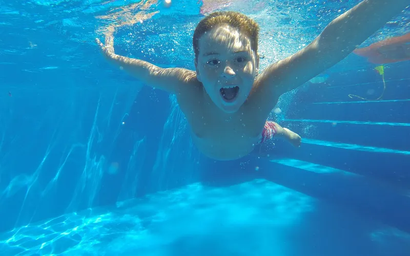 Kind taucht lachend mit ausgebreiteten Armen durch ein Schwimmbecken
